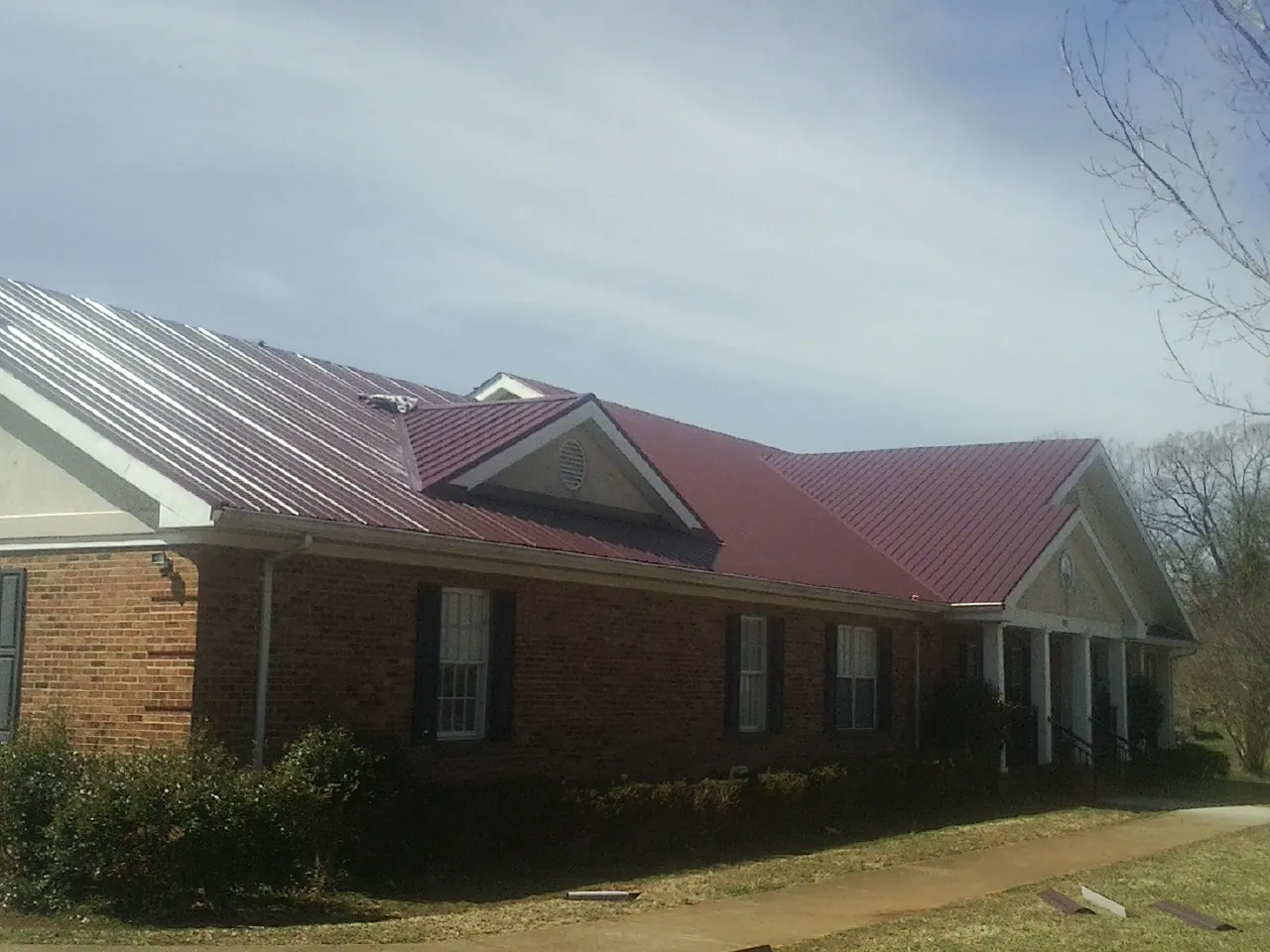 Red metal roof with gabled entries on a long brick building, from a Hail Damage Roof Repair job in Gainesville